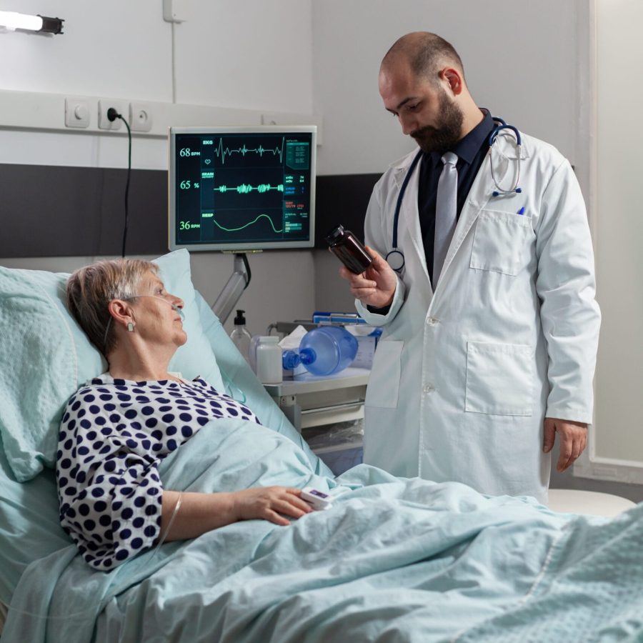 Senior woman patient breathing with help from oxygen tube laying in hospital bed, listening doctor explaying diagnosis treatmant holding pills bottle for recovery.
